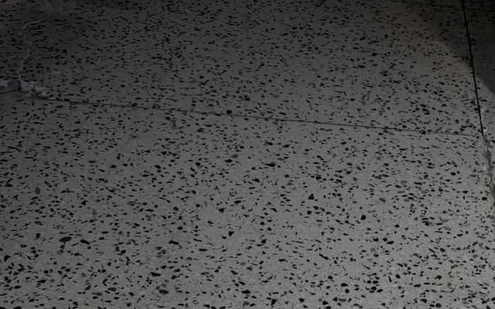 Sliten terrazzo med svarta och grå stenkorn inför slipning